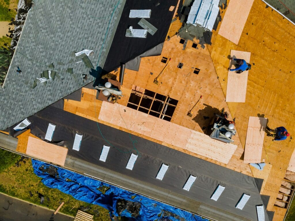 A roofer nailing shingles with air gun, replacing roof cover protection being applied