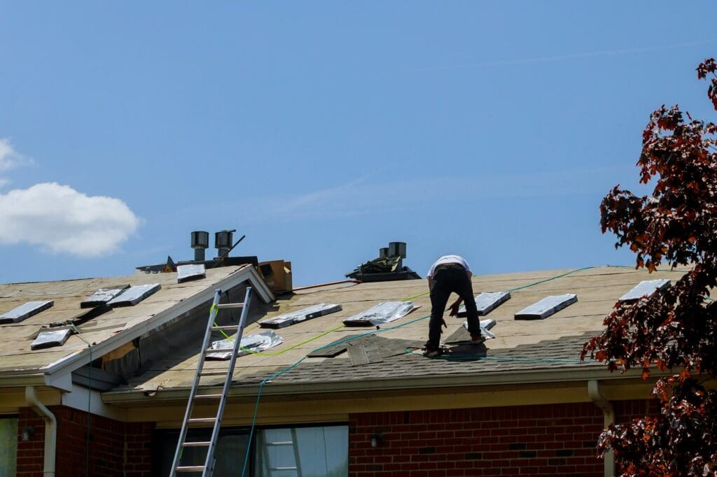 Roof repair, worker with replacing gray tiles shingles on house being applied new braunfels