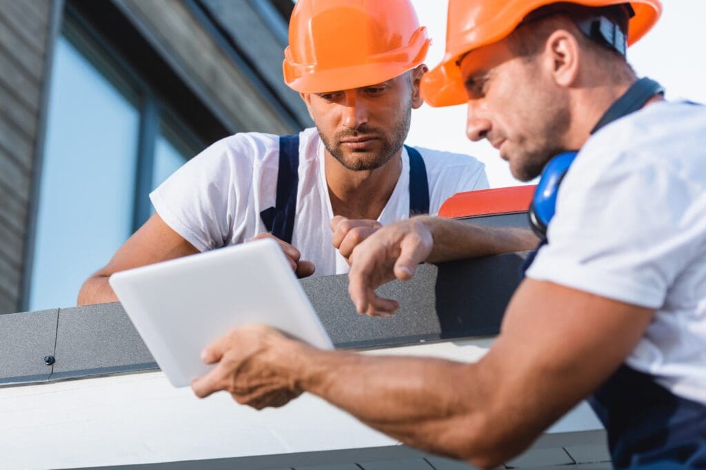 Selective focus of manual workers looking at digital tablet on roof of house